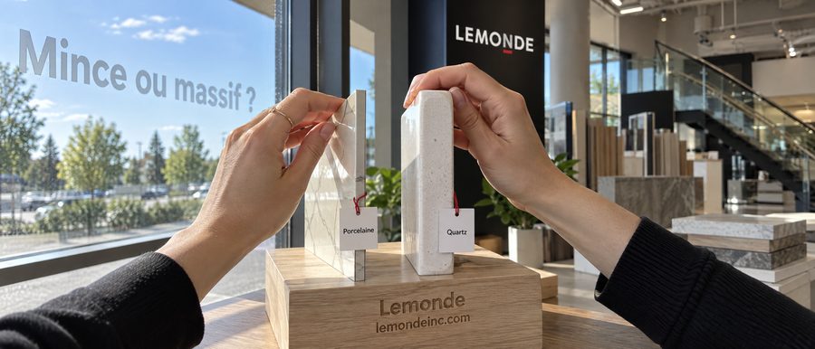 Deux mains comparent le rebord mince d'une dalle de porcelaine et le rebord épais d'un quartz, près d'une fenêtre ensoleillée du showroom de Boucherville